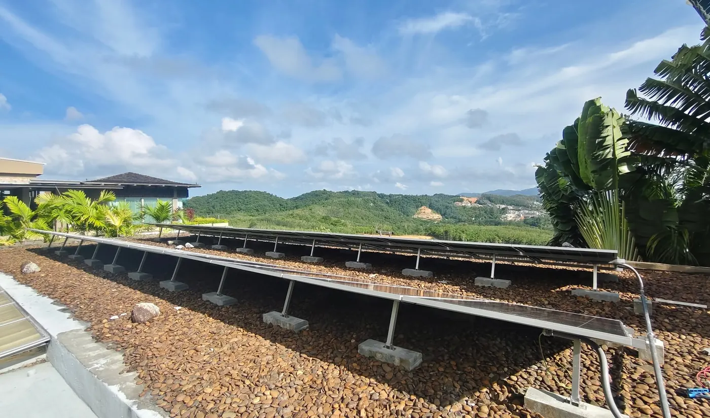 แผงโซล่าเซลล์ของระบบไฮบริด 15.48 kW ตั้งบนโครงฐานคอนกรีตบนดาดฟ้าปูหินกรวดของพูลวิลล่าในภูเก็ต