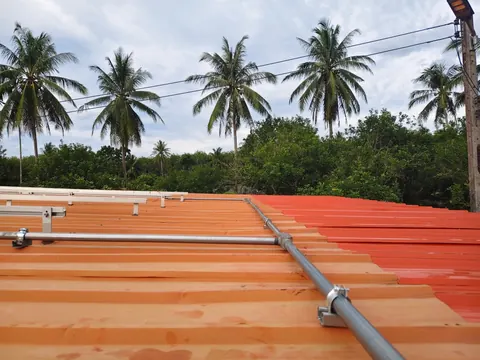 ท่อร้อยสายไฟเดินบนหลังคาเมทัลชีทสีส้ม ท่ามกลางสวนมะพร้าว