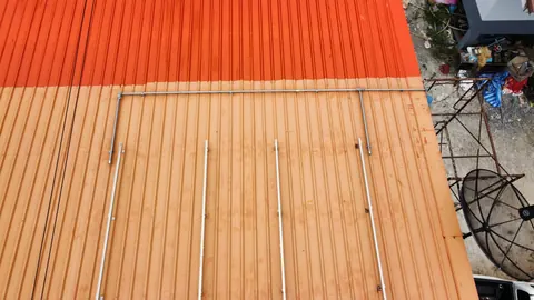 ระยะใกล้หลังคาเมทัลชีทสีส้มพร้อมท่อร้อยสายไฟจากระบบโซล่าเซลล์