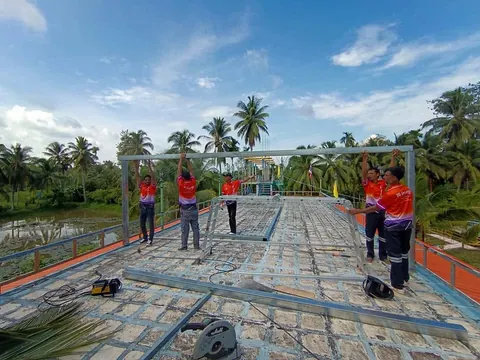 ทีมช่างชุดส้มทำงานบนโครงหลังคาระหว่างติดตั้งระบบโซล่าเซลล์
