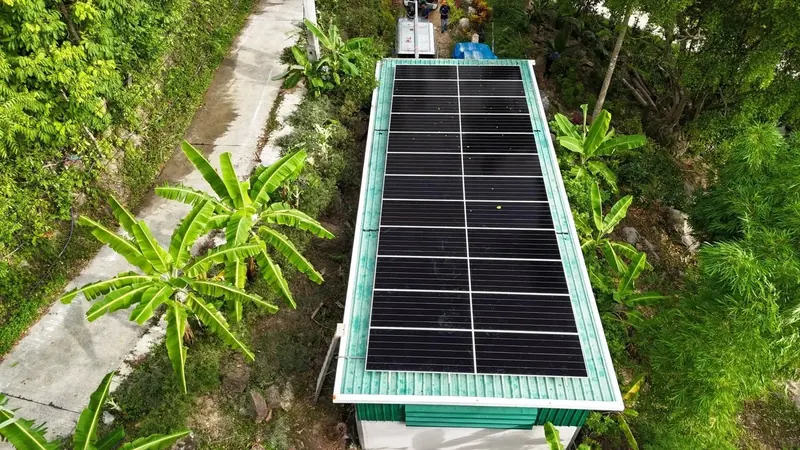 Aerial view of a long, narrow roof with solar panels amid green surroundings