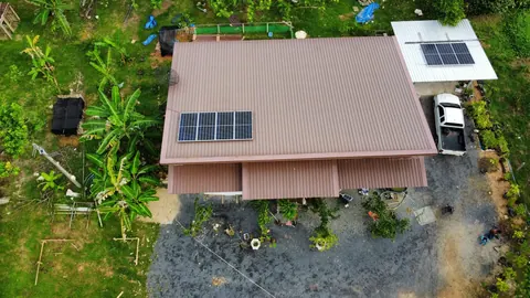 ภาพมุมสูงบ้านหลังคาสีน้ำตาลติดแผงโซล่าเซลล์กลางสวน