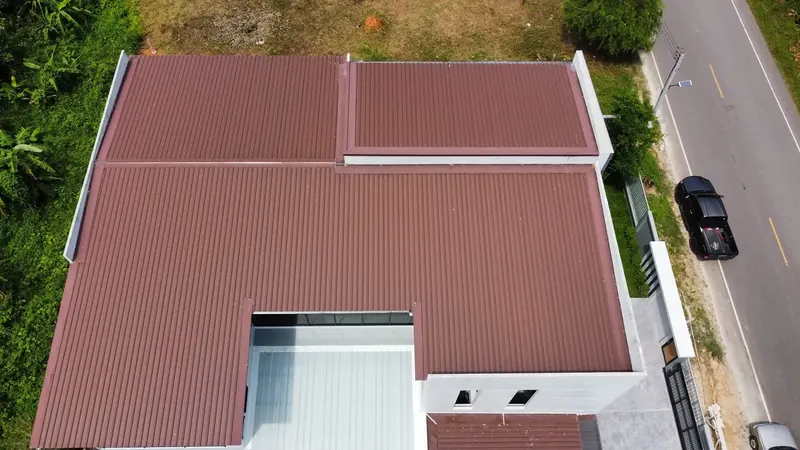 Aerial view of a reddish-brown-roofed house with solar panels beside a road