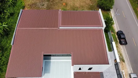ภาพมุมสูงบ้านหลังคาสีน้ำตาลแดงติดแผงโซล่าเซลล์ริมถนน
