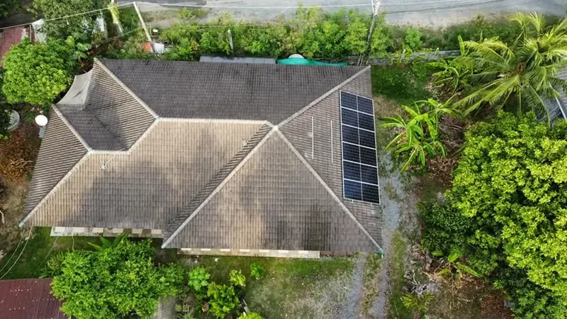 ภาพมุมสูงบ้านหลังคาปั้นหยาที่ติดแผงโซล่าเซลล์ ล้อมรอบด้วยต้นไม้ใหญ่