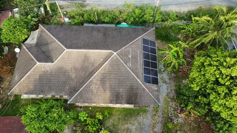 ภาพมุมสูงบ้านหลังคาปั้นหยาที่ติดแผงโซล่าเซลล์ ล้อมรอบด้วยต้นไม้ใหญ่