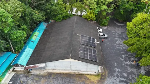 ภาพมุมสูงหลังคาบ้านที่ติดแผงโซล่าเซลล์ ล้อมรอบด้วยป่าเขียวทึบ