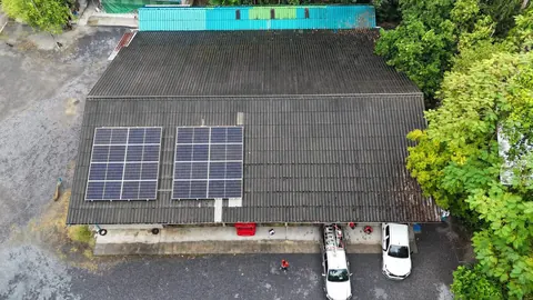 ภาพมุมสูงบ้านหลังคาสีเทาที่ติดแผงโซล่าเซลล์ มีรถจอดอยู่หน้าบ้าน