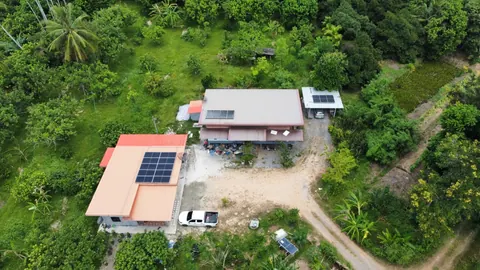 ภาพมุมสูงบ้านหลังคาสีส้มที่ติดแผงโซล่าเซลล์ กลางสวนยางพารา
