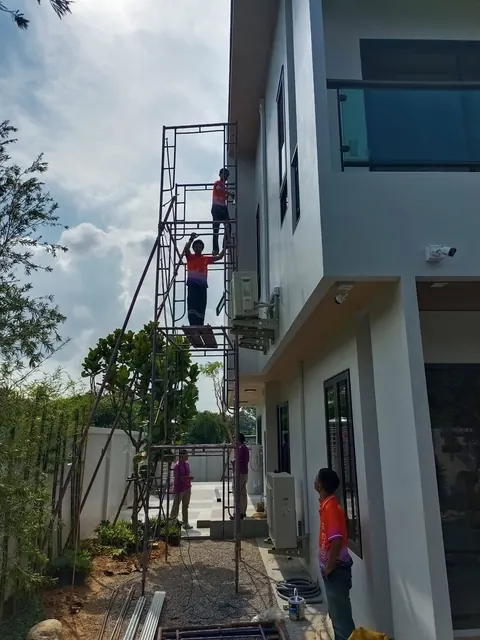 ช่างขึ้นนั่งร้านเดินระบบไฟฟ้าข้างผนังอาคารสองชั้น
