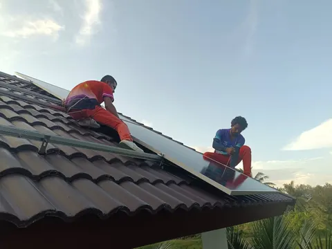 ช่างสองคนกำลังยกและจัดวางแผงบนหลังคากระเบื้องลอนของบ้านพักอาศัย