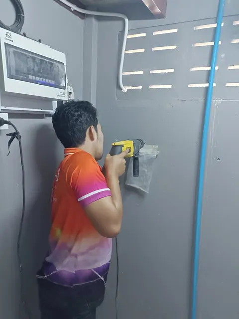 ช่างกำลังตรวจสอบตู้ควบคุมไฟฟ้าที่ติดตั้งบนผนังภายนอกอาคาร