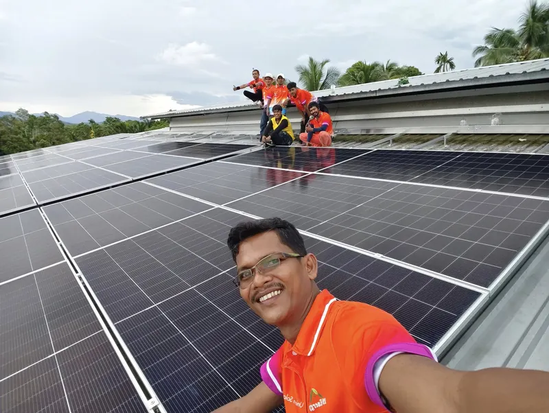 Khun Chokchai, owner of 19 Energy, on a roof with the solar panels in place, with the technicians in orange team shirts behind